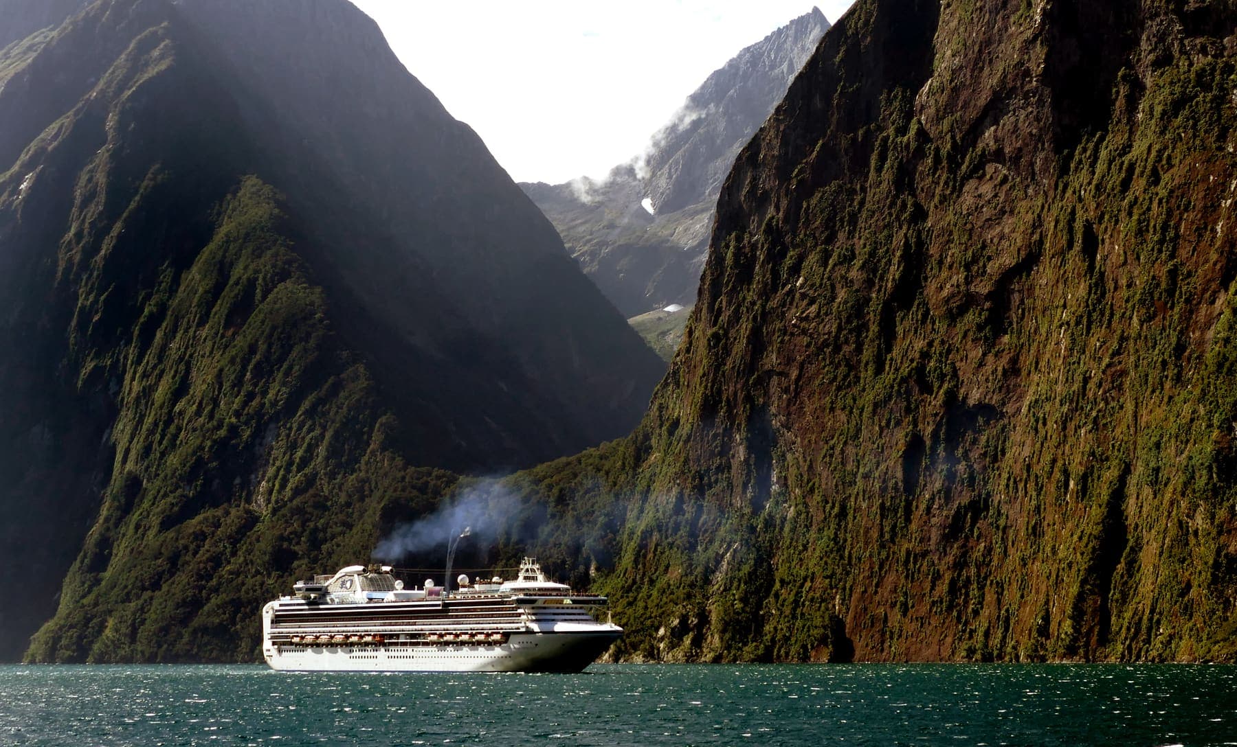 A cruise ship sailing through Milford Sound beneath steep, forested fiord walls